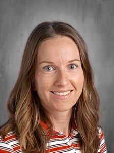 Headshot of a woman with long brown hair, smiling, wearing a striped shirt, with a neutral background.