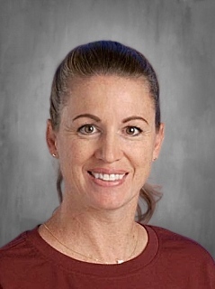 Smiling woman with brown hair in a ponytail, wearing a maroon shirt, against a gray background.