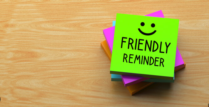 Bright sticky notes stacked on a wooden surface, with a green note saying "Friendly Reminder" and a smiley face.