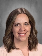 Headshot of a woman with shoulder-length brown hair, smiling, wearing a light pink blouse against a gray background.