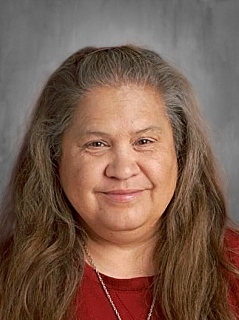 A person with long hair smiling, wearing a red top against a gray background.