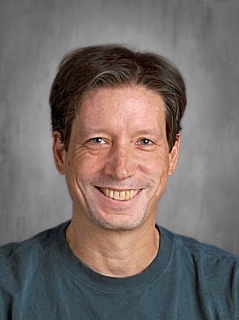 Smiling person with short hair wearing a gray shirt, set against a plain gray background.